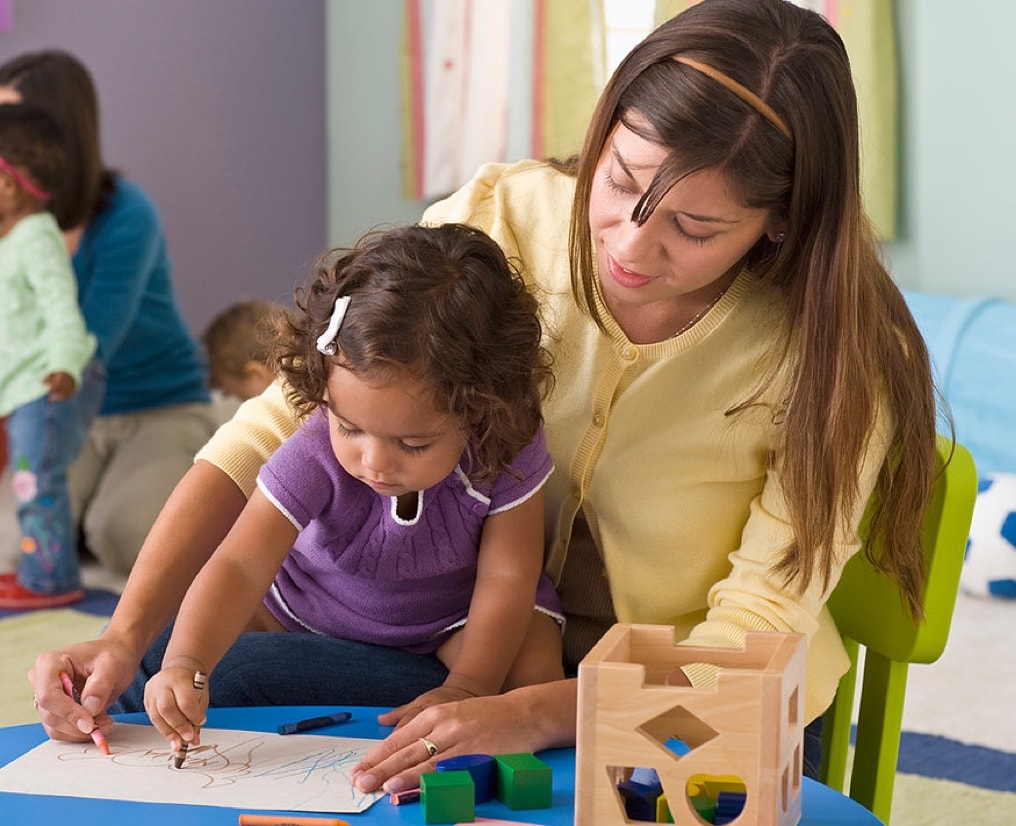 Young girl and her teacher drawing with crayons.