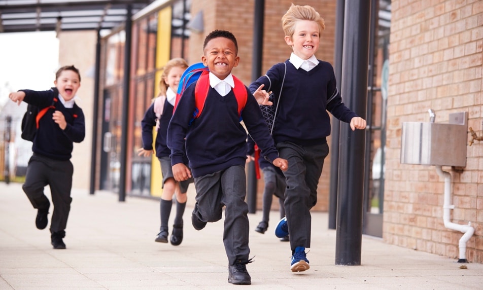Smiling children in school uniforms running outside.