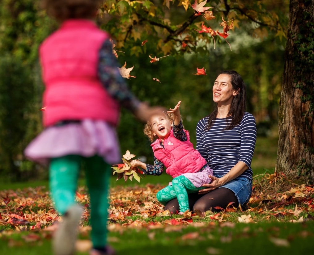 Girl joyously playing with leaves in a park.